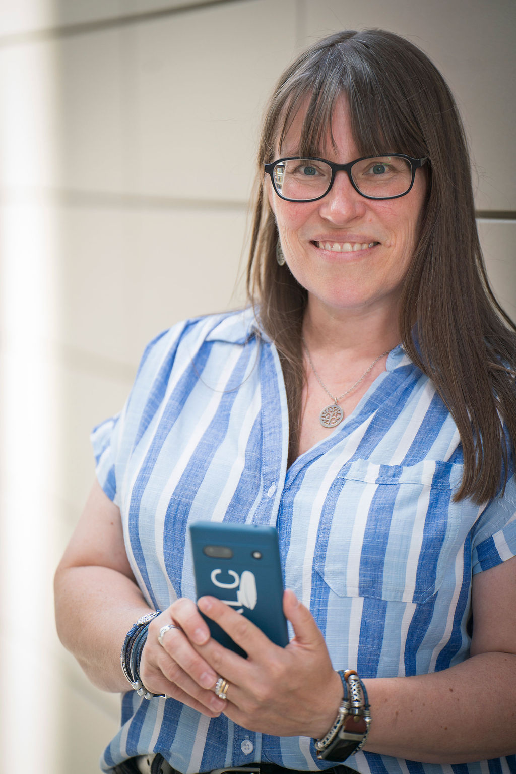 RLCwordsCopywriterBrandPhotographybySuzanneKentish0075 Rebecca Chamberlain head and shoulders wearing a blue striped shirt and glasses, and holding a blue phone with RLC Words logo