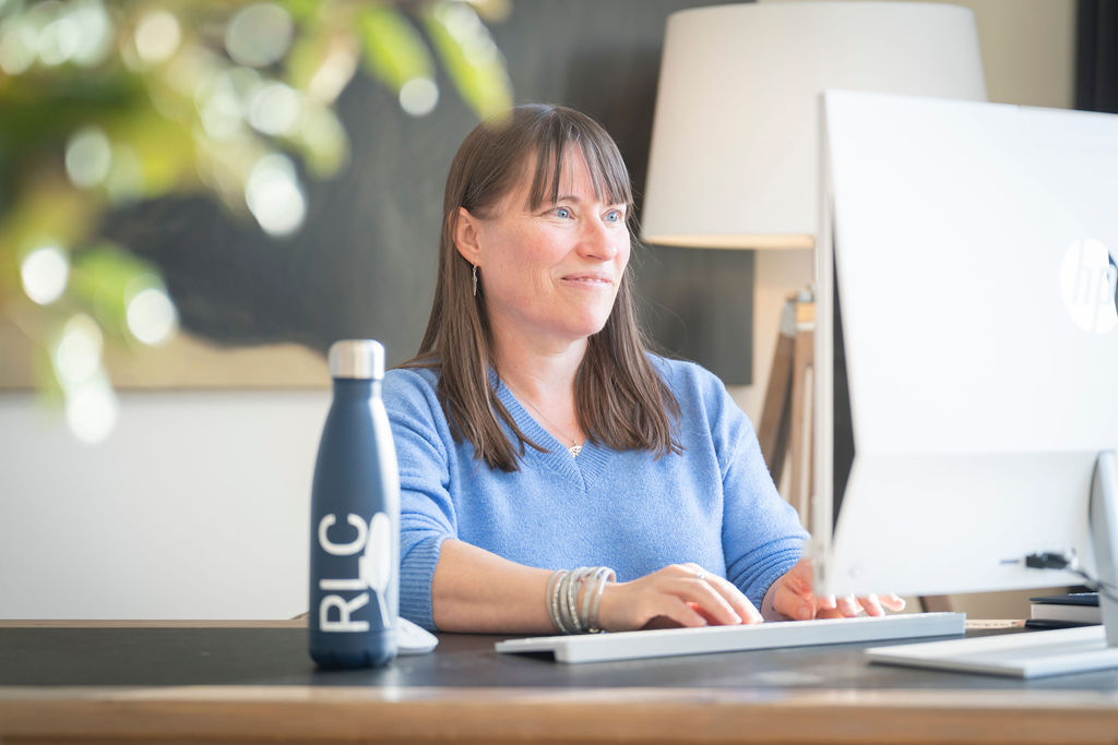 Rebecca Chamberlain typing on a laptop with RLC Words bottle beside